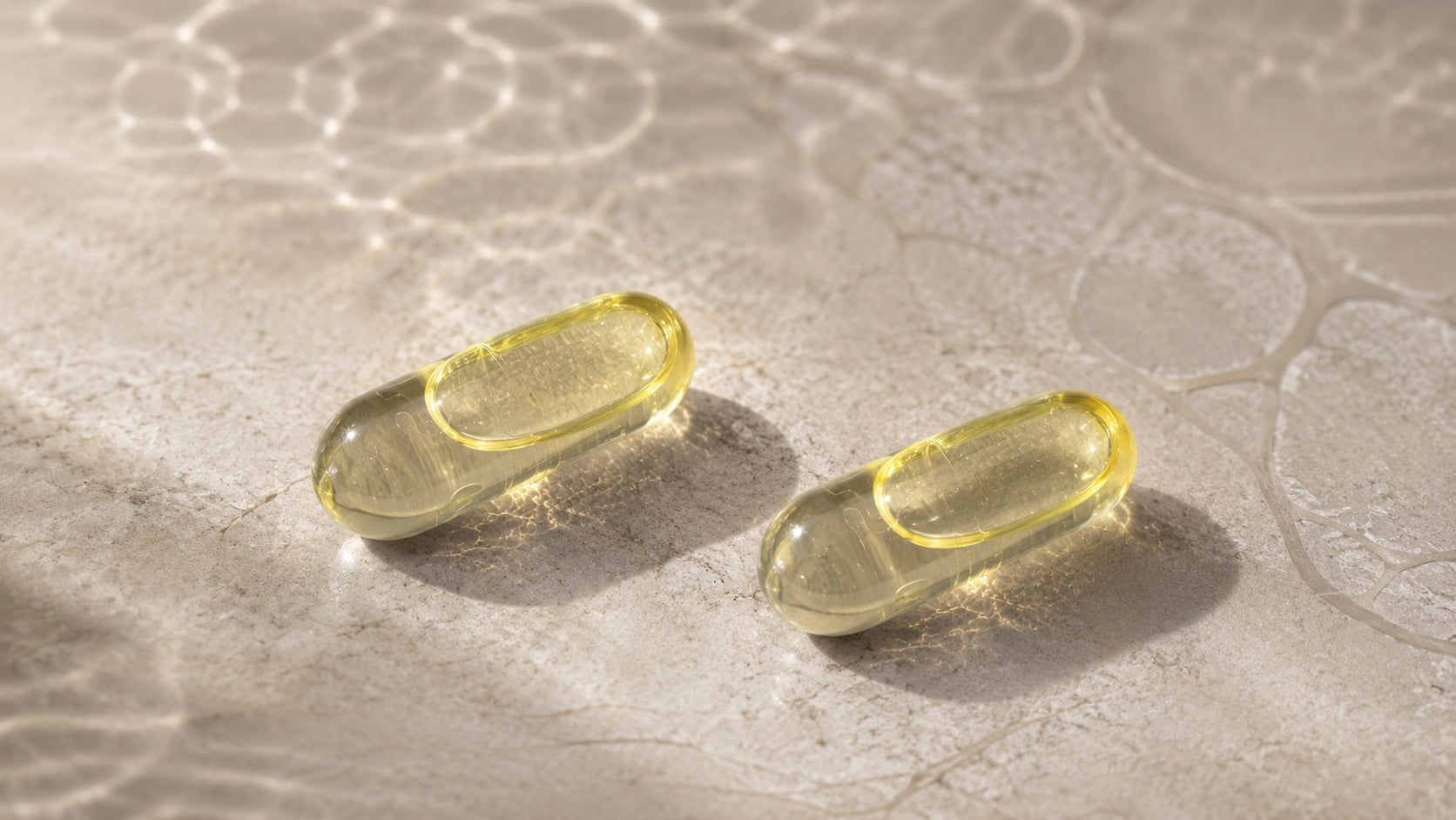 Zwei transparente HPMC Liquid-Caps mit hell goldfarbenem Algenöl auf mineralischem Untergrund.