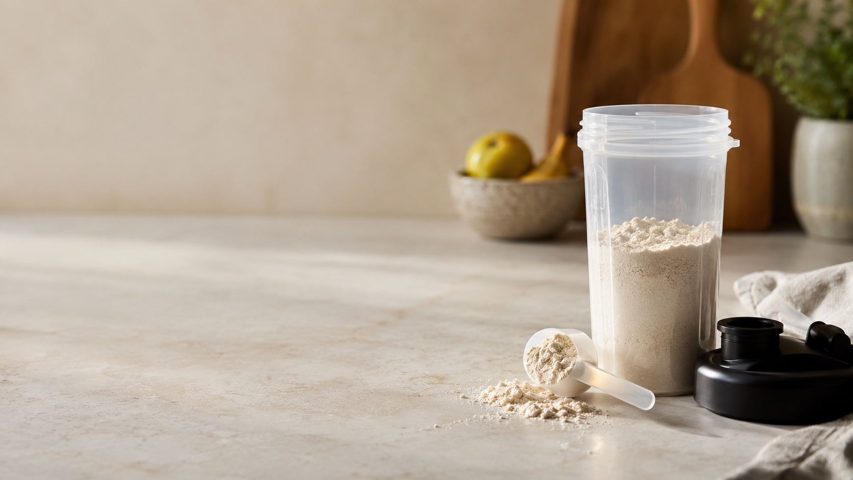 Offener Shaker mit Proteinpulver und Messlöffel auf einem hellen Küchentresen.
