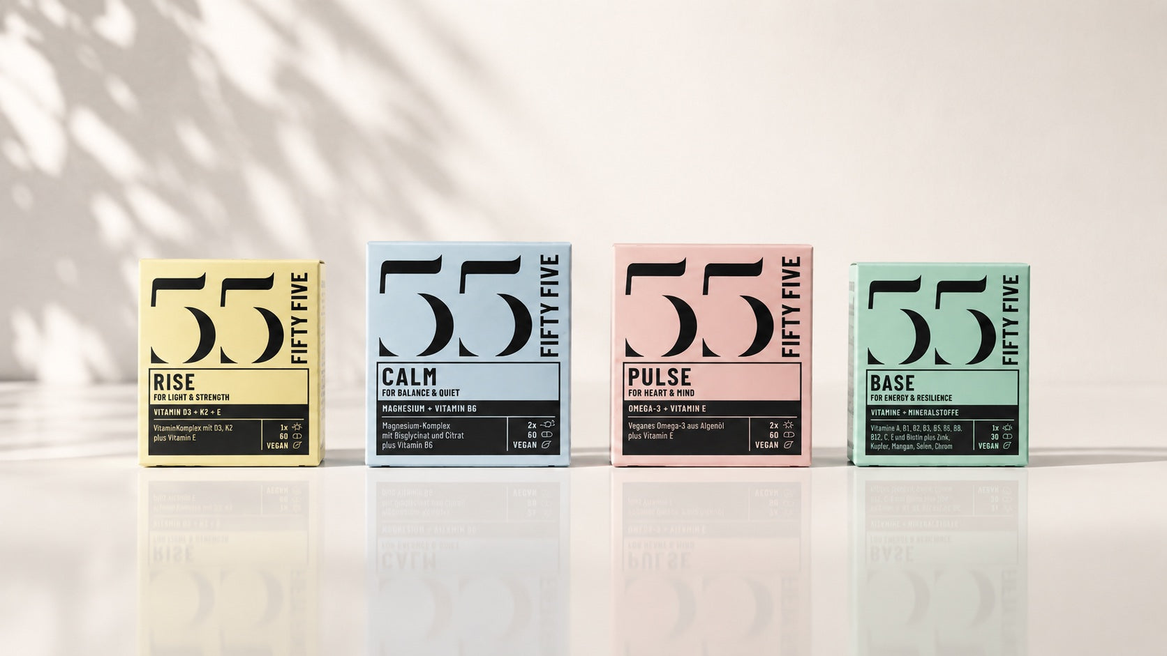 Fifty Five Daily Essentials Set mit vier farblich einzigartigen Supplement Boxen auf heller, leicht reflektierender Oberfläche.