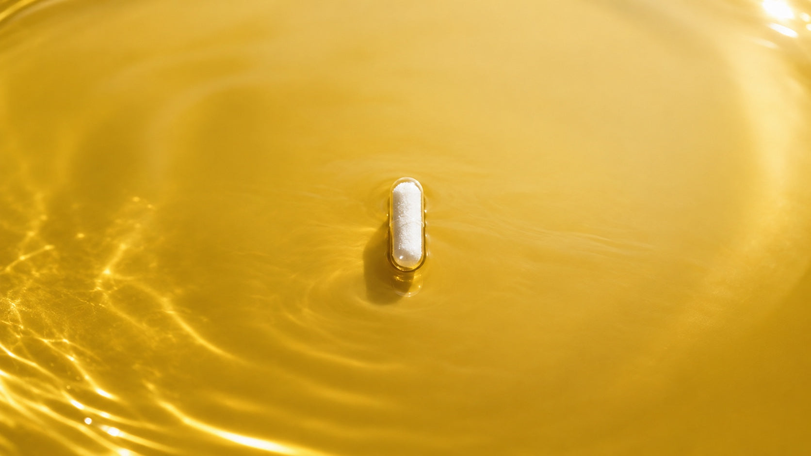 Kleine transparente HPMC Micro-Kapsel mit weißem Pulver liegt in einer glatten goldgelben Ölfläche mit feinem Lichtspiel.