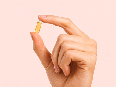 Goldene PULSE Omega-3 Liquid-Kapsel von Fifty Five zwischen Daumen und Zeigefinger